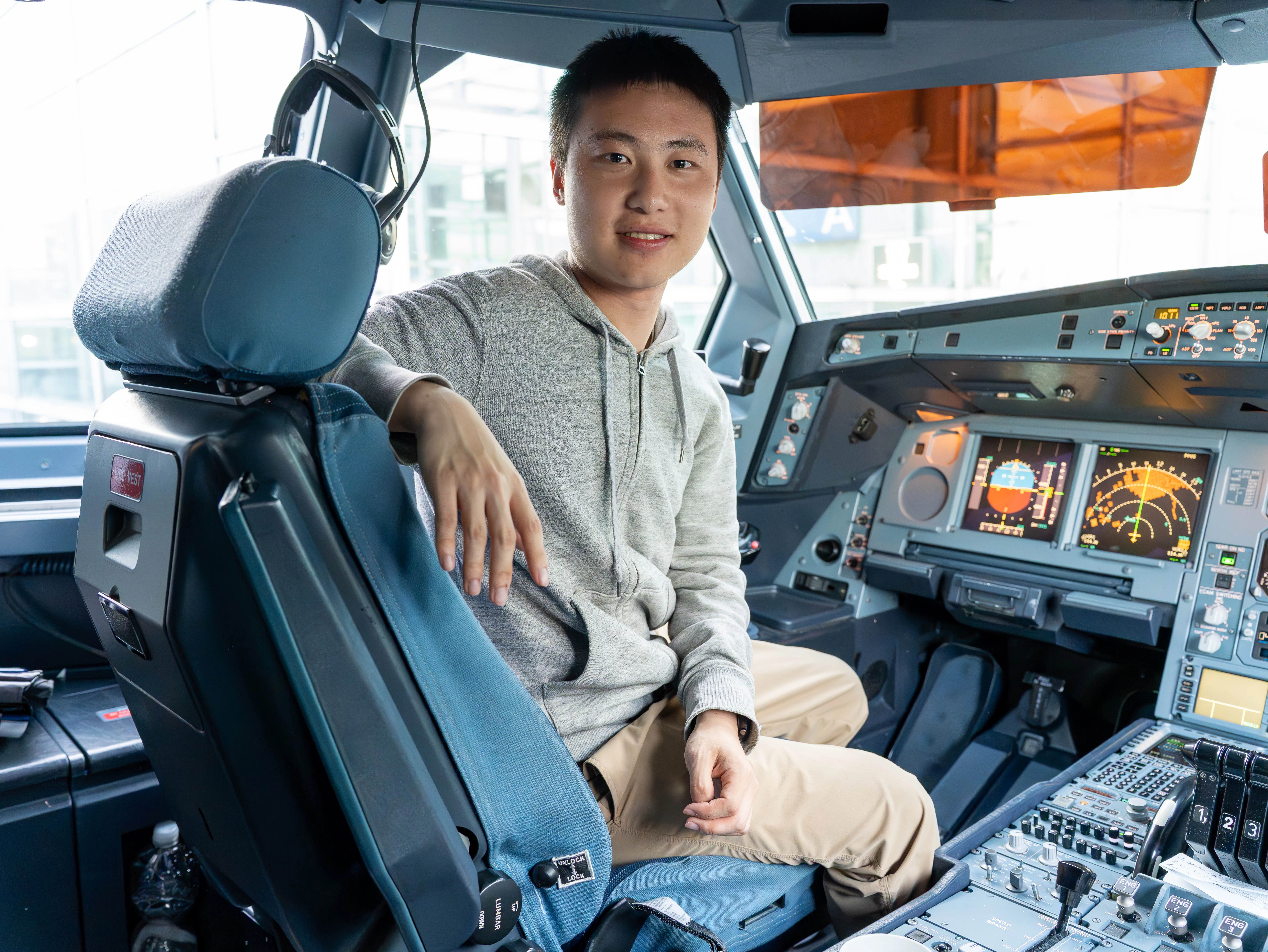 The author smiling in the captain&rsquo;s seat of the A340-600 cockpit, next to the primary flight and navigation displays