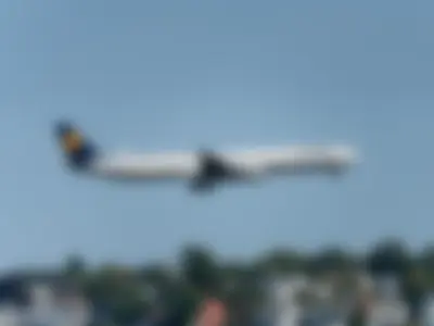 Lufthansa A340-600 in the classic livery on final approach with gear down, above a row of houses and trees