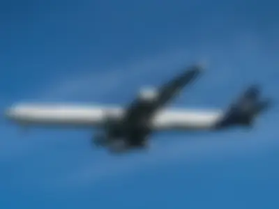 Underside view of a Lufthansa A340-600 in the new livery against a deep blue sky, showing all four engines and the landing gear