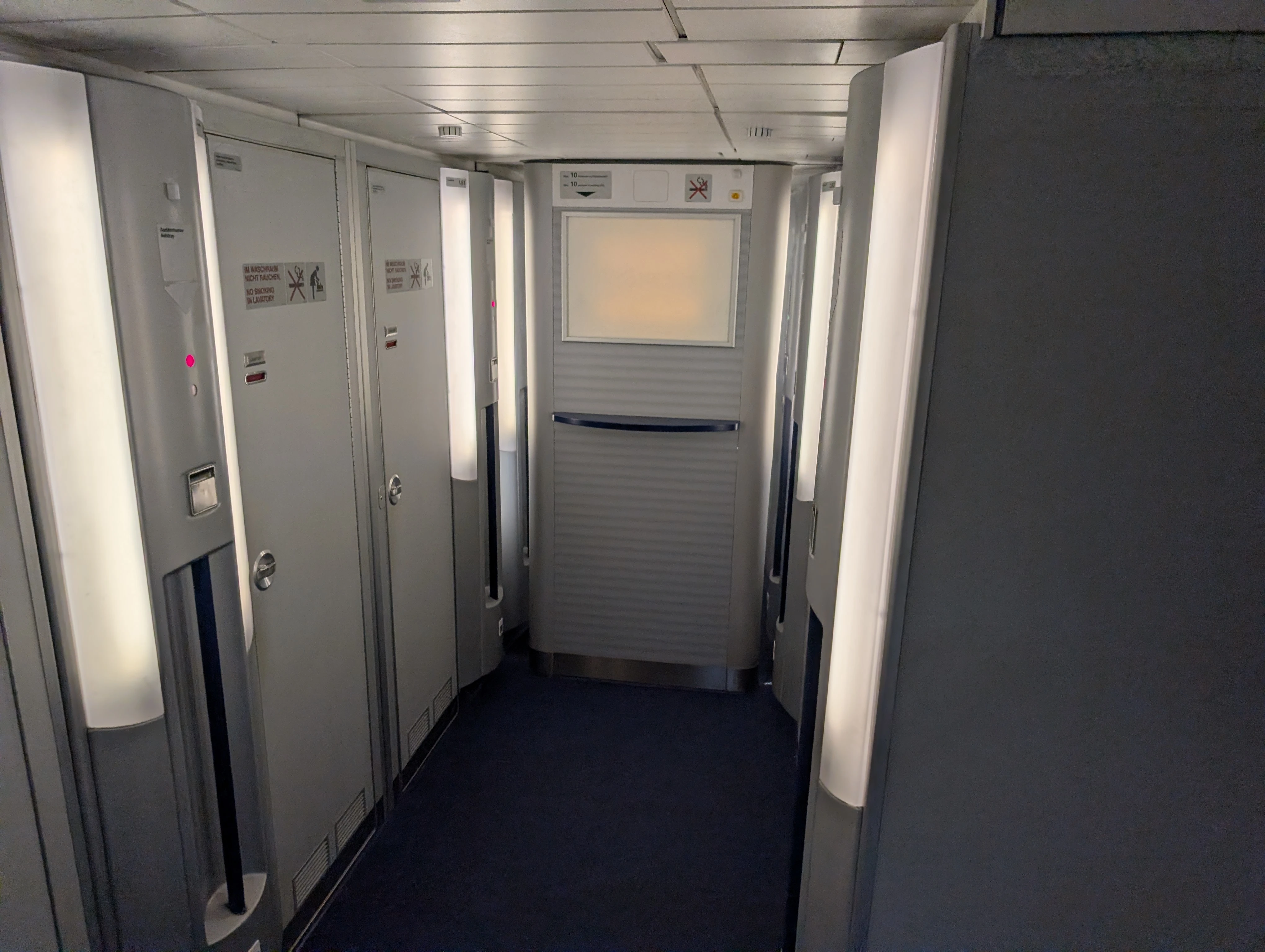A lower-deck corridor lined with lavatories on both sides, lit by tall vertical light panels
