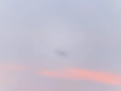 The A340-600 seen from behind as a small silhouette with four engines, flying away above pink streaks of cloud