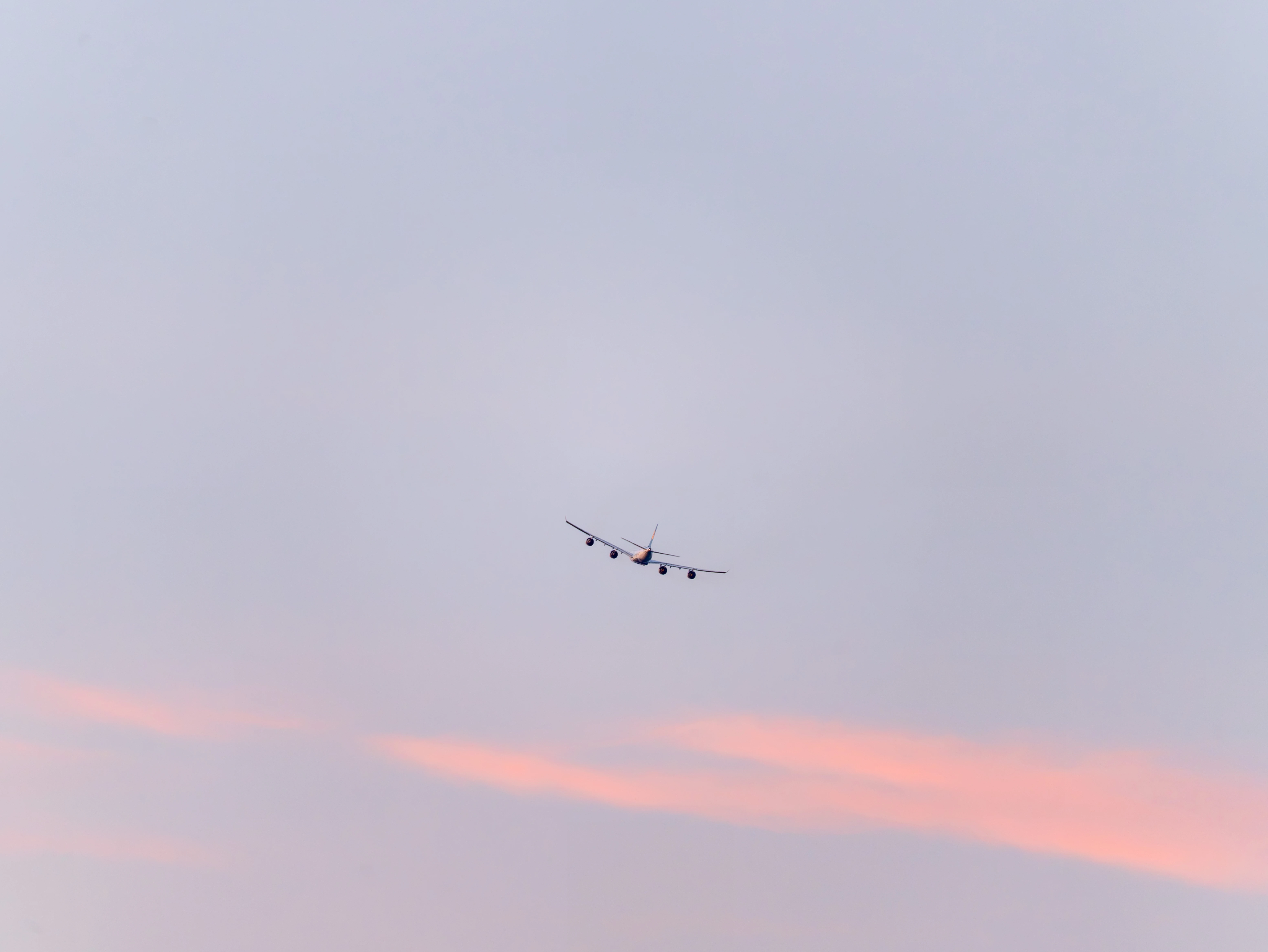 The A340-600 seen from behind as a small silhouette with four engines, flying away above pink streaks of cloud
