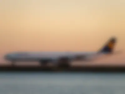 Side profile of the long Lufthansa A340-600 on the runway against a peach-coloured evening sky above the water
