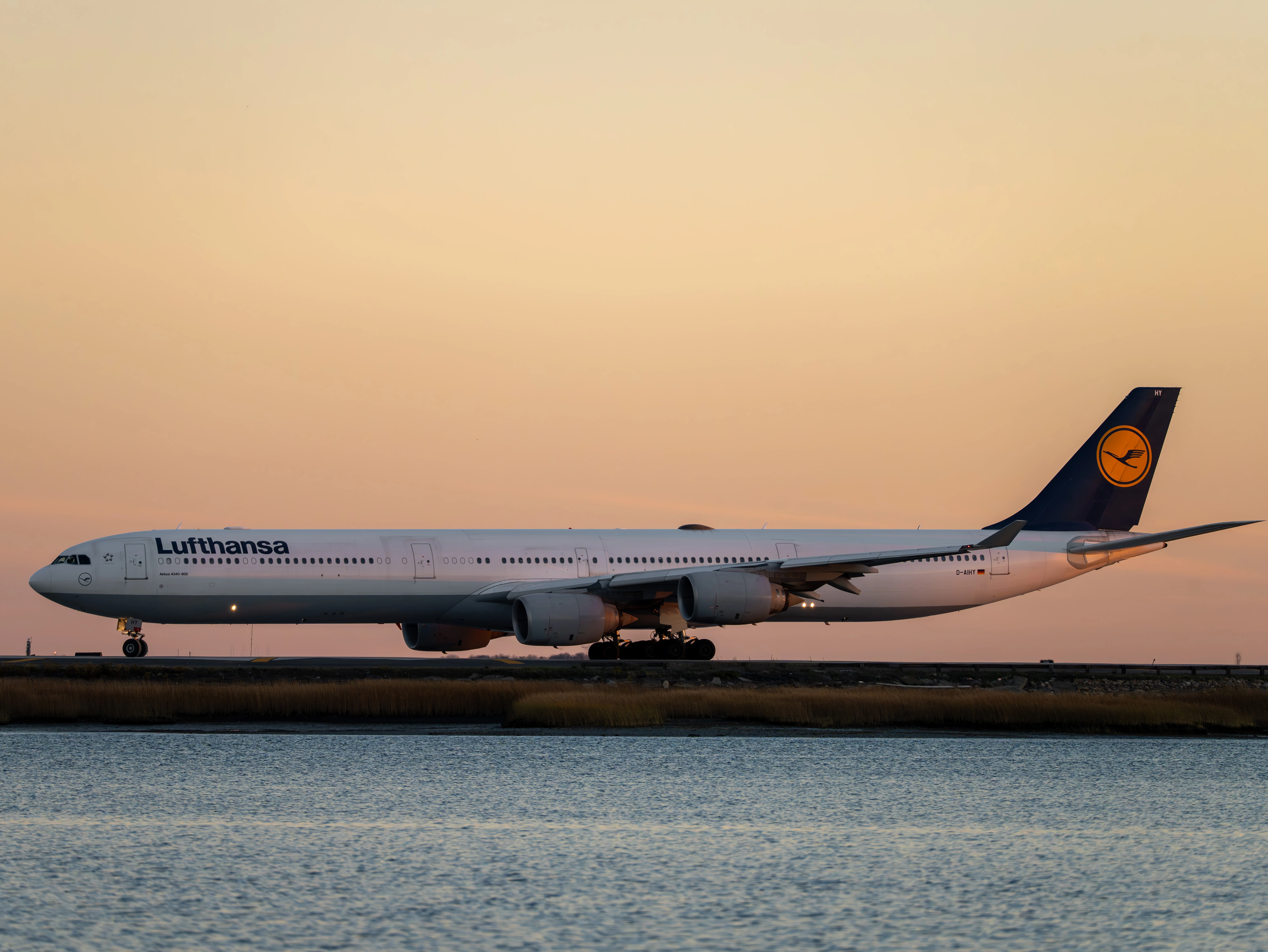 Side profile of the long Lufthansa A340-600 on the runway against a peach-coloured evening sky above the water