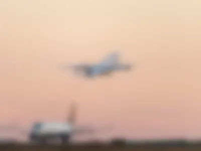 Lufthansa A340-600 climbing steeply into the pink twilight sky while a Delta regional jet waits on the ground