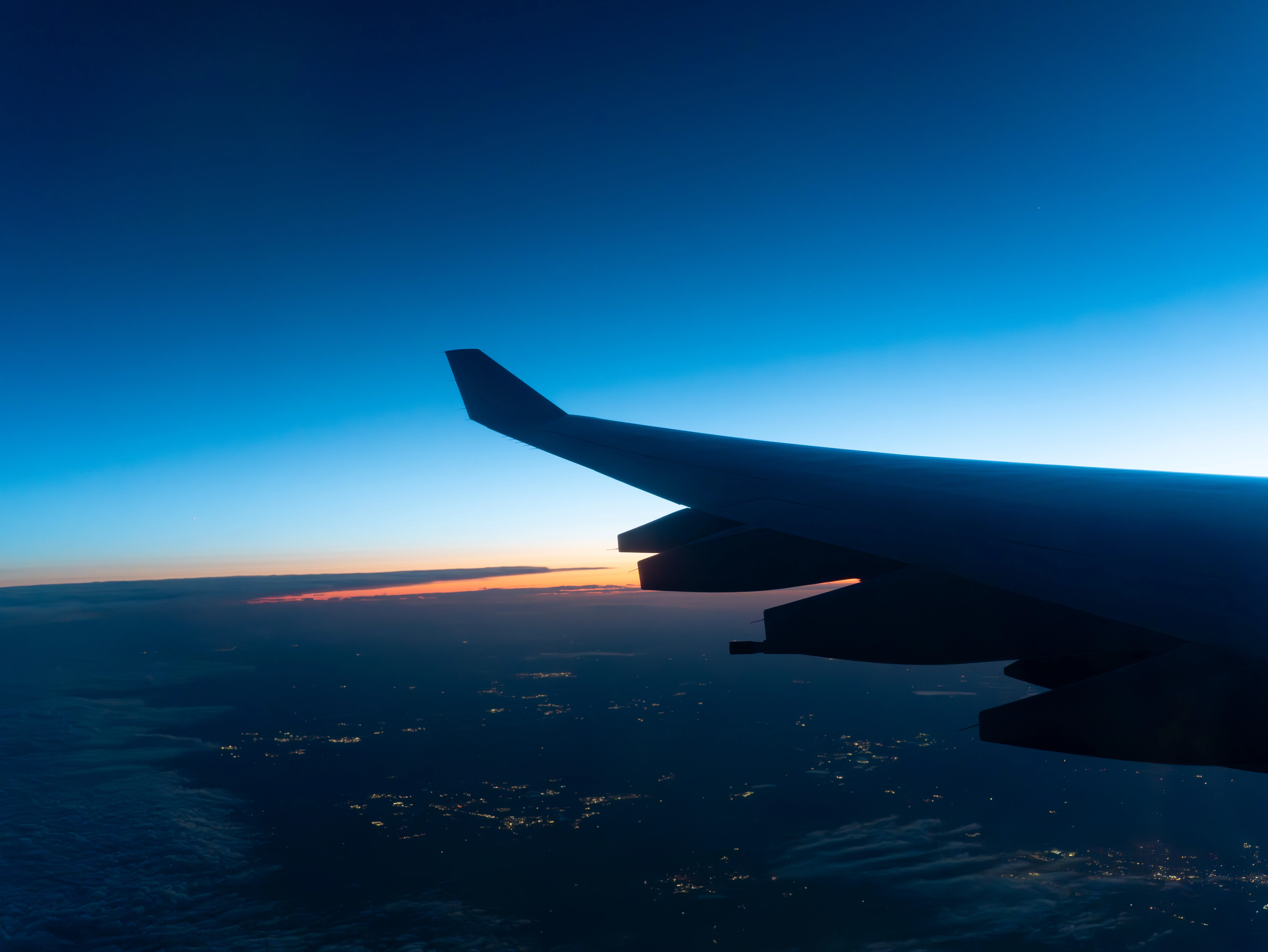 Silhouette of the A340-600 wing against a deep blue sky at dawn, with a thin orange horizon and city lights below