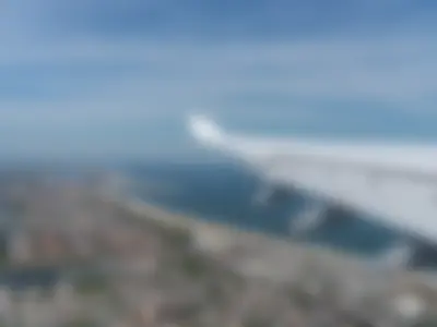 View from the cabin window of the A340-600 wing over a coastal town, a long sandy beach, and the ocean