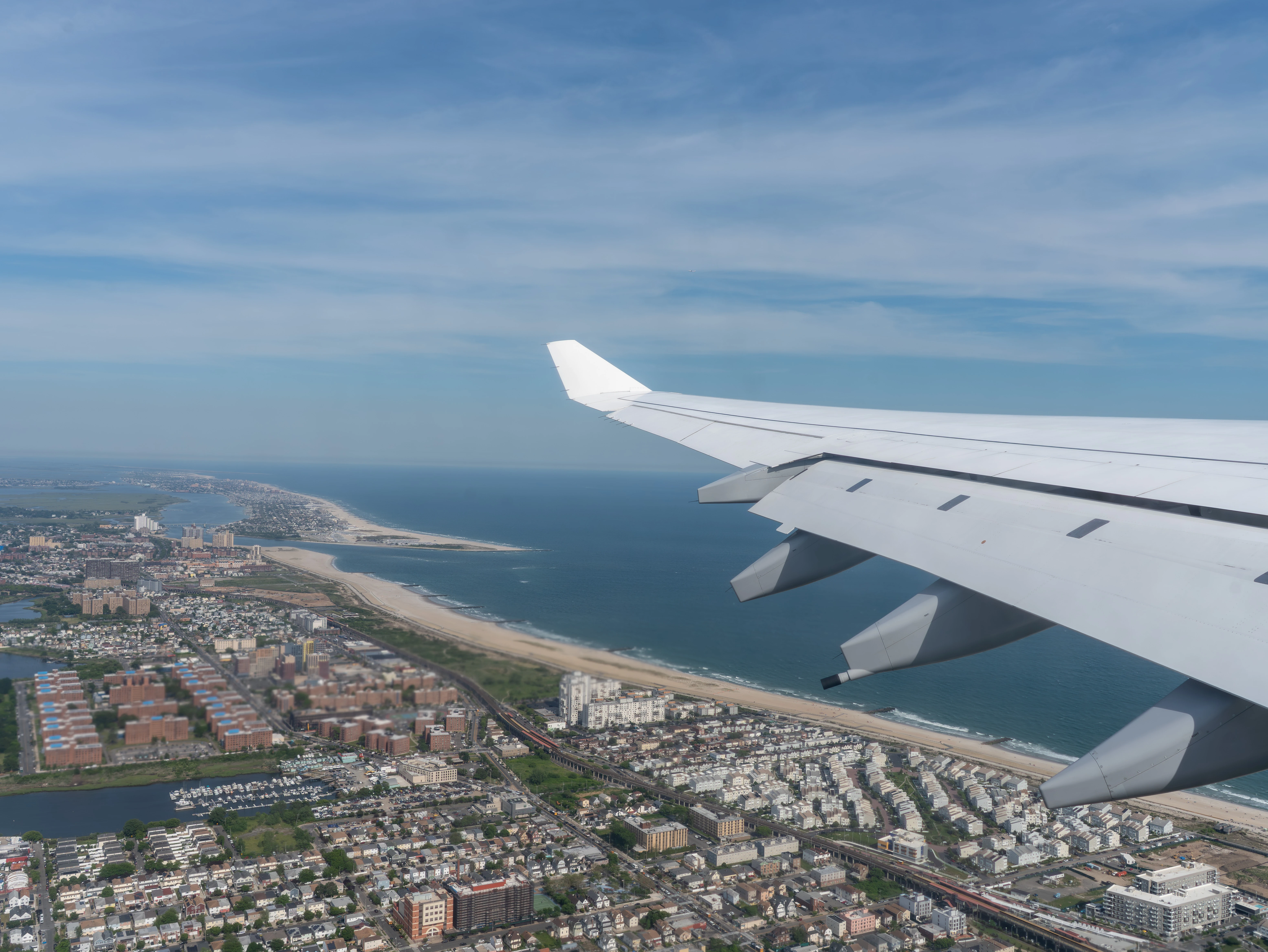 View from the cabin window of the A340-600 wing over a coastal town, a long sandy beach, and the ocean